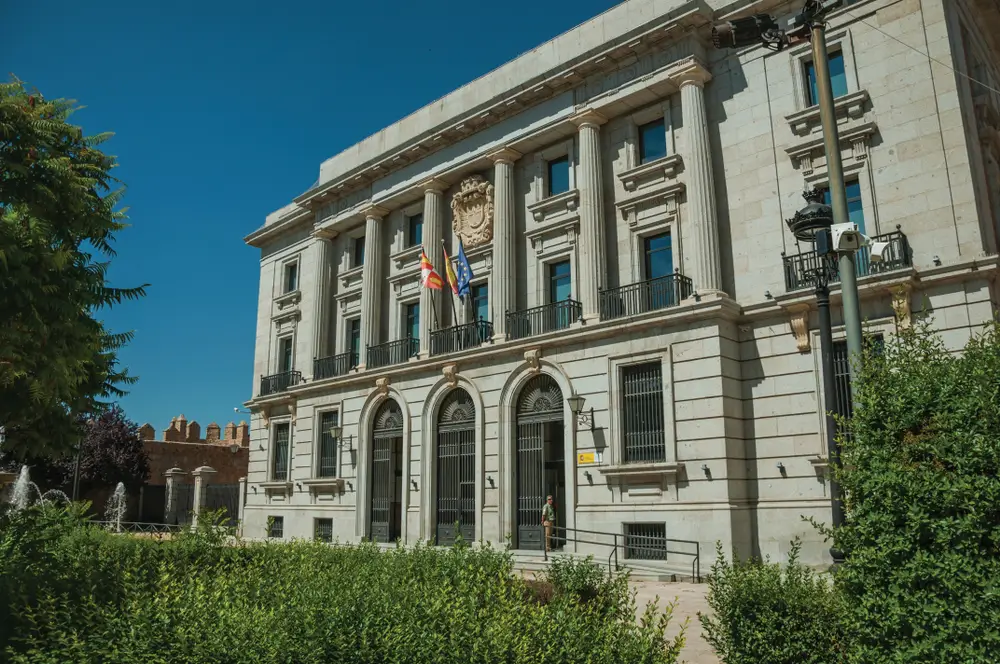 Fachada del edificio oficial de la Escuela Nacional de Policía en Ávila con columnas, banderas y jardines.