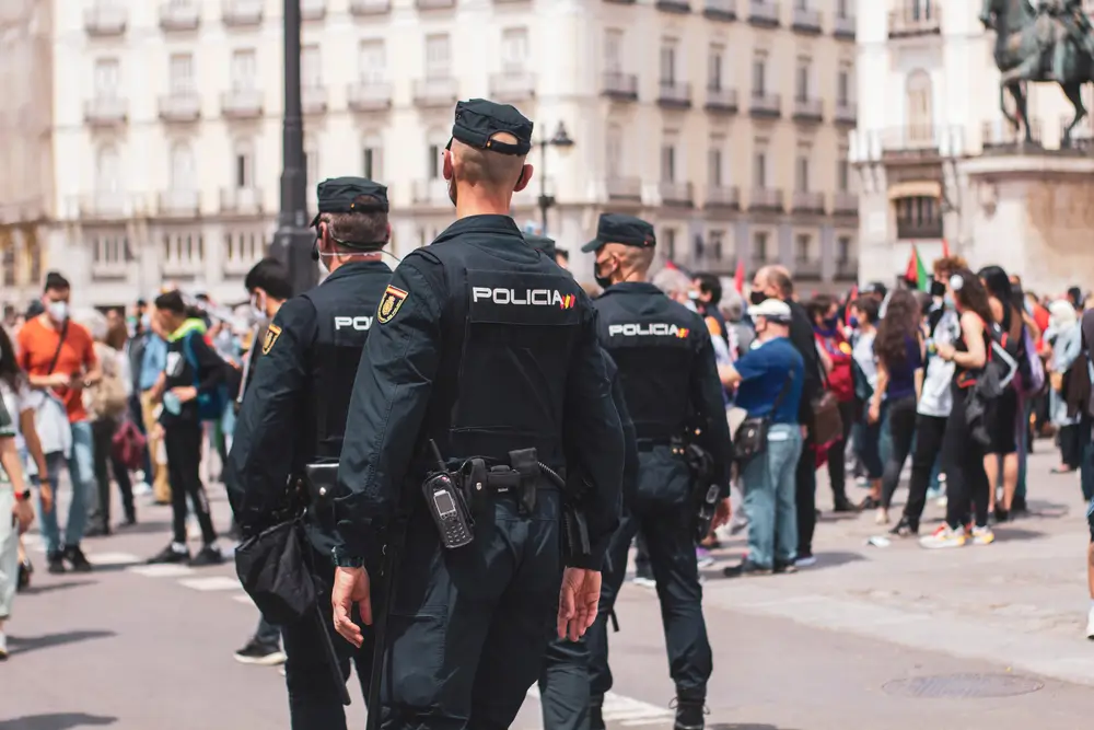 Agentes de la Policía Nacional de espaldas patrullando una plaza concurrida en un entorno urbano.