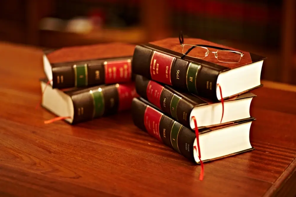 Libros de derecho y códigos penales apilados con unas gafas sobre una mesa de madera para estudiar el temario jurídico.