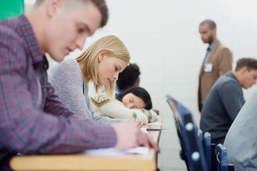 Aspirantes a policía concentrados realizando un examen en un aula bajo la supervisión de un examinador.