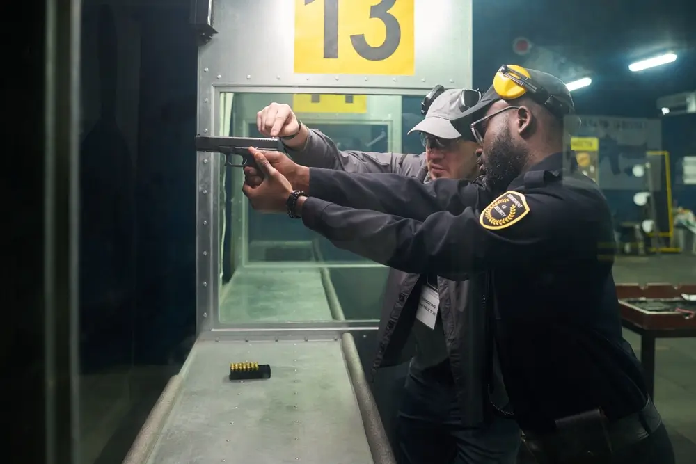 Instructor de policía impartiendo formación profesional técnica de tiro a un agente en una galería de entrenamiento.
