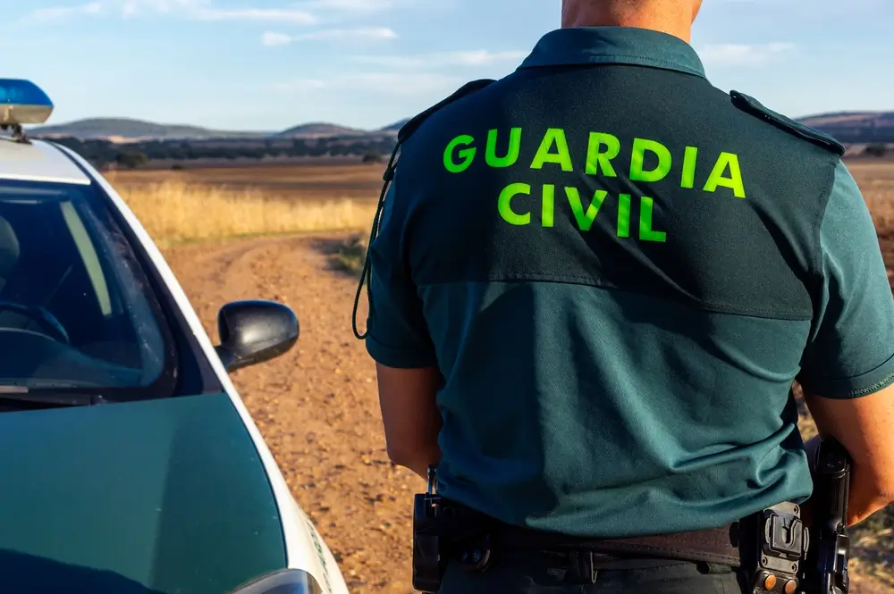 Agente de la Guardia Civil de espaldas durante una patrulla rural junto a un vehículo oficial en campo abierto.