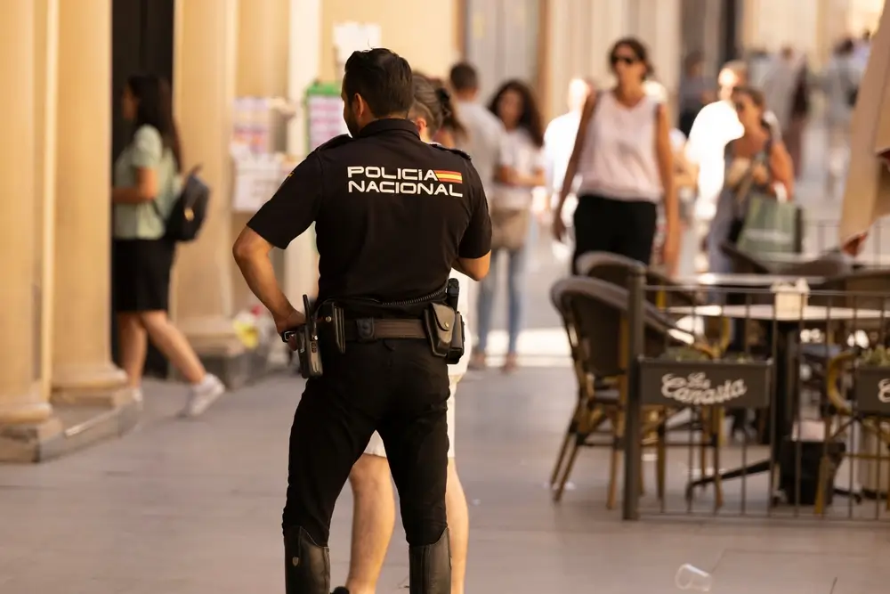 Agente de la Policía Nacional de espaldas con su uniforme reglamentario patrullando una zona urbana concurrida.