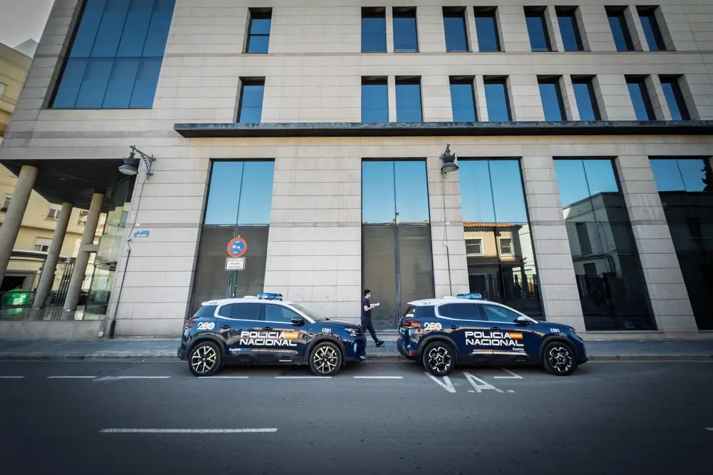 Dos coches patrulla de la Policía Nacional estacionados frente a un edificio administrativo en una zona urbana.