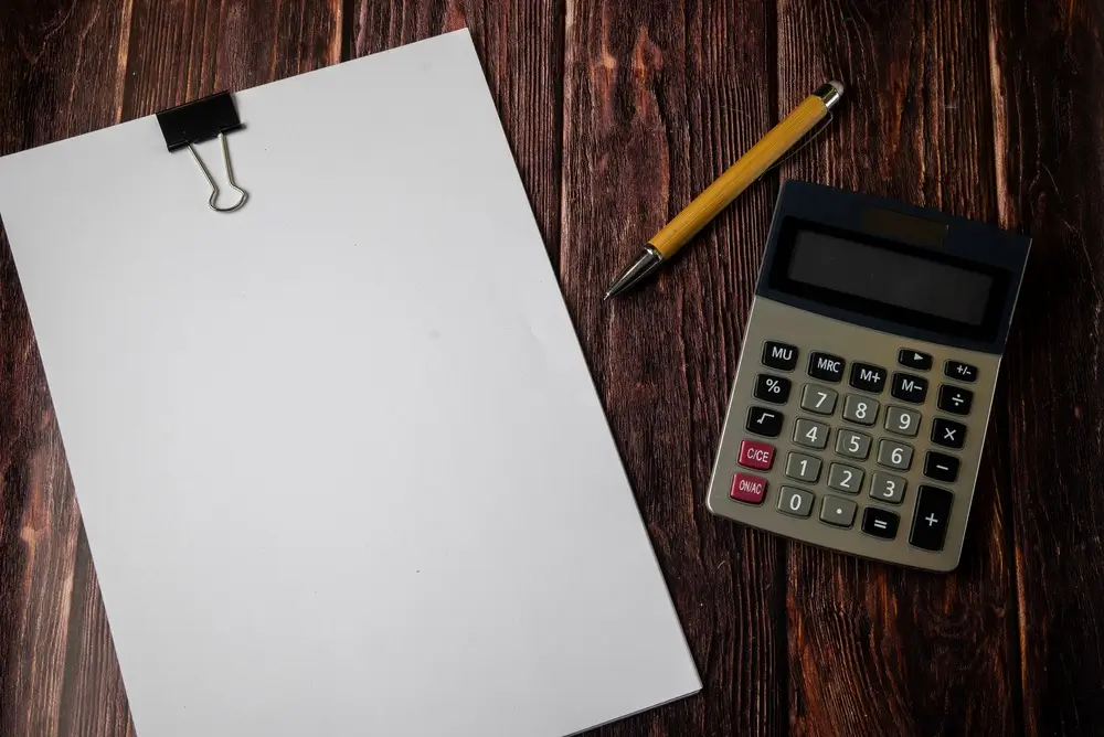 Bolígrafo y calculadora sobre una mesa de madera para calcular los resultados de un simulacro de examen psicotécnico.