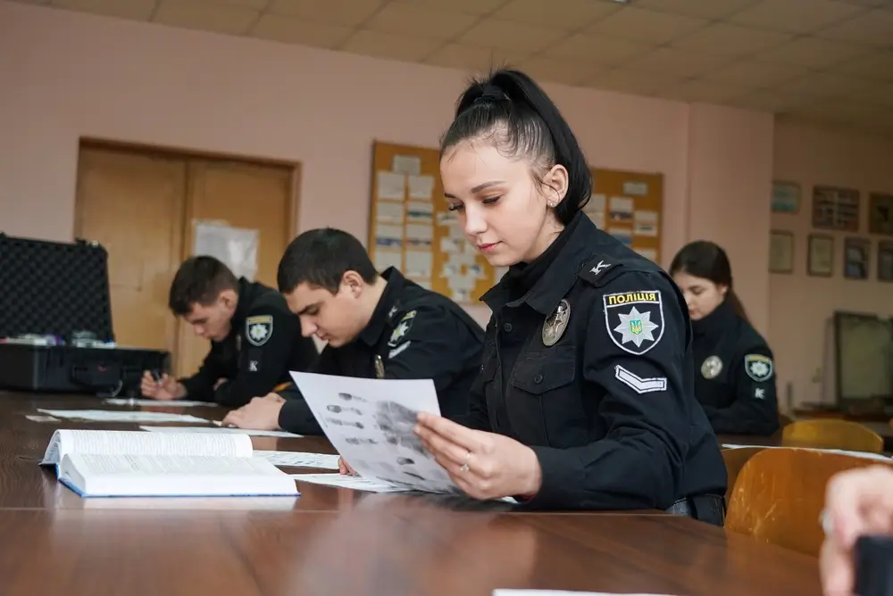 Alumna policía uniformada en clase de formación técnica analizando huellas dactilares en el aula.
