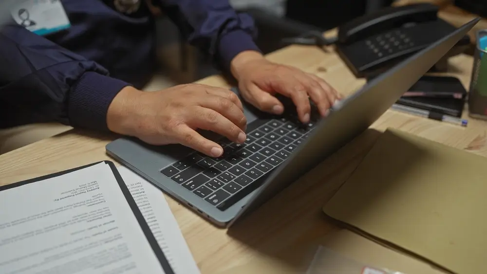 Agente de policía trabajando con un portátil en una oficina de comisaría, realizando tareas de gestión y planificación.