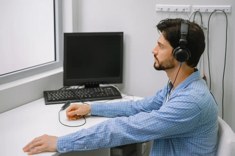 Hombre realizando una prueba de audiometría clínica con auriculares y equipo médico para una revisión de audición.